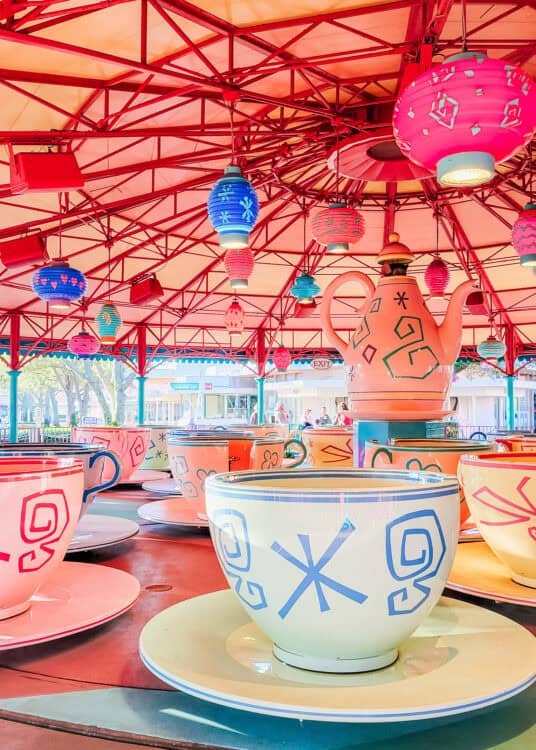 Colorful teacup ride vehicles under a pink roof hung with colorful lanterns