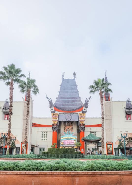 Chinese Theatre entrance to Mickey and Minnies Runaway Railway at Disneyโs Hollywood Studios framed by tall palm trees. The colorful attraction marquee hangs beneath the ornate pagoda style roof.