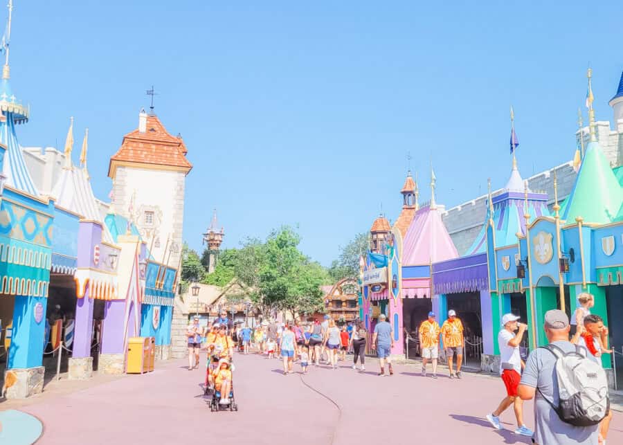 Sidewalk in Disney World's Fantasyland with just a handful of people walking on it. On either side you see colorful medieval fair like facades for the ride buildings