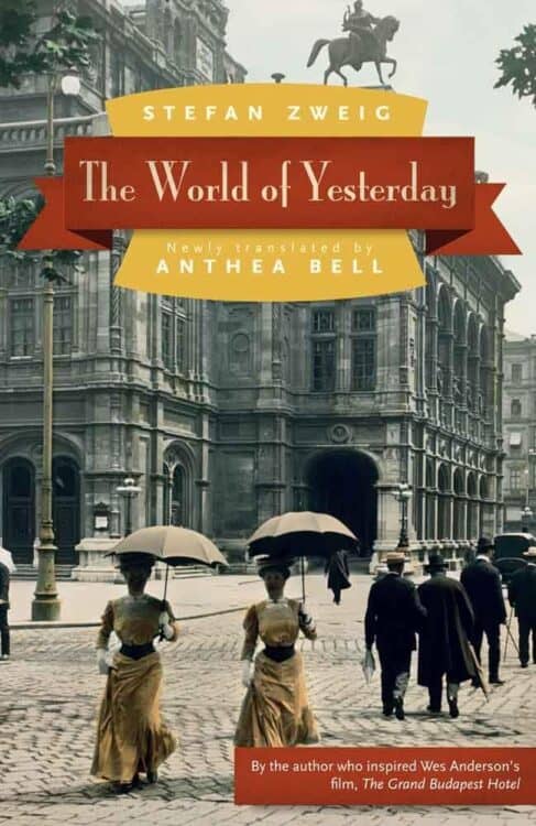 Cover of The World of Yesterday by Stefan Zweig, newly translated by Anthea Bell, featuring a vintage street scene with women in long dresses and hats holding parasols as they walk past a grand European building. A red and yellow banner displays the title, with a note at the bottom referencing the author's influence on Wes Anderson’s The Grand Budapest Hotel.