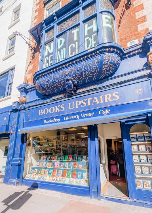 Exterior of Books Upstairs in Dublin, a vibrant blue independent bookshop with gold lettering and a window display filled with colorful book covers. The ornate blue Victorian-style facade adds character to the historic storefront.