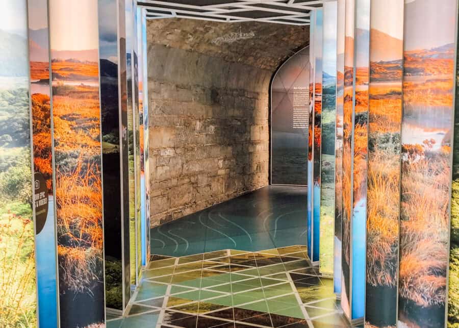 Colorful entrance hallway at EPIC The Irish Emigration Museum in Dublin, with mirrored panels displaying vivid landscapes of Ireland and a geometric floor pattern leading into a stone-arched corridor. The immersive design invites visitors into an interactive exhibit space.