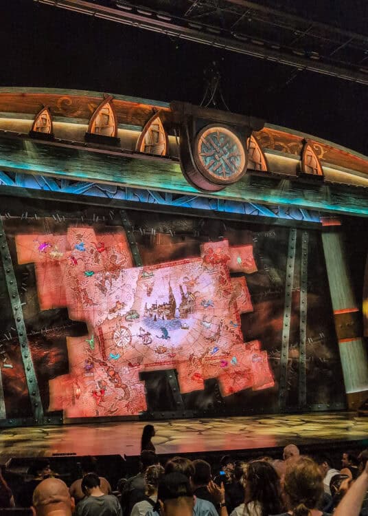 Indoor stage show at Universal Studios with a large glowing map projection featuring dragons and fantasy illustrations displayed across a wide set. Guests sit in rows facing the stage as part of an immersive show experience that adds variety beyond rides for kids at Universal Studios.