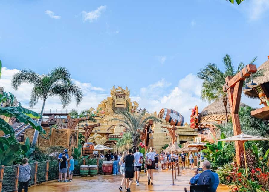 Entrance to a tropical themed Donkey Kong Mine Cart Madness ride at Universal Studios with a large stone temple facade and palm trees lining the walkway. Families walk toward the attraction through a colorful jungle setting that highlights a fun ride for kids at Universal Studios.