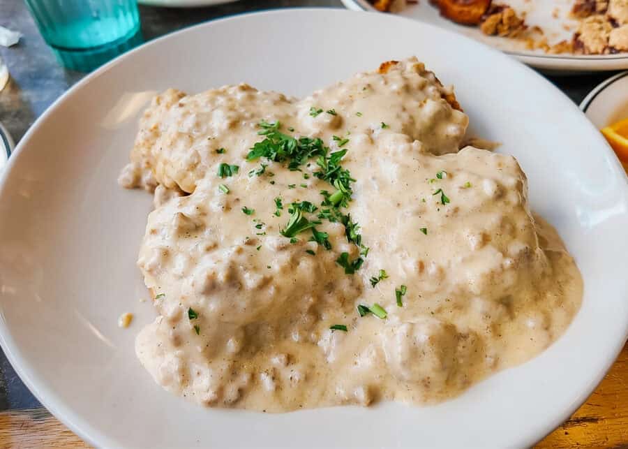 Fluffy biscuits covered in thick creamy sausage gravy and topped with chopped fresh parsley. The classic biscuits and gravy breakfast is served on a large white plate.