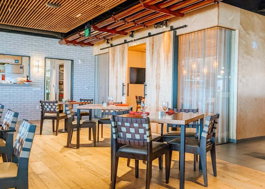 Modern hotel restaurant dining area with wood floors and tables set with wine glasses and red napkins. Woven chairs and large sliding wood doors complement the warm contemporary interior.