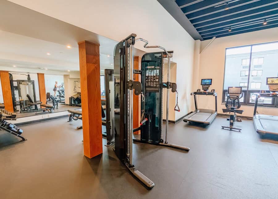 Modern hotel fitness center with a Precor cable weight machine. Treadmills. Stationary bike. Free weights. Exercise benches. And a mirrored wall.